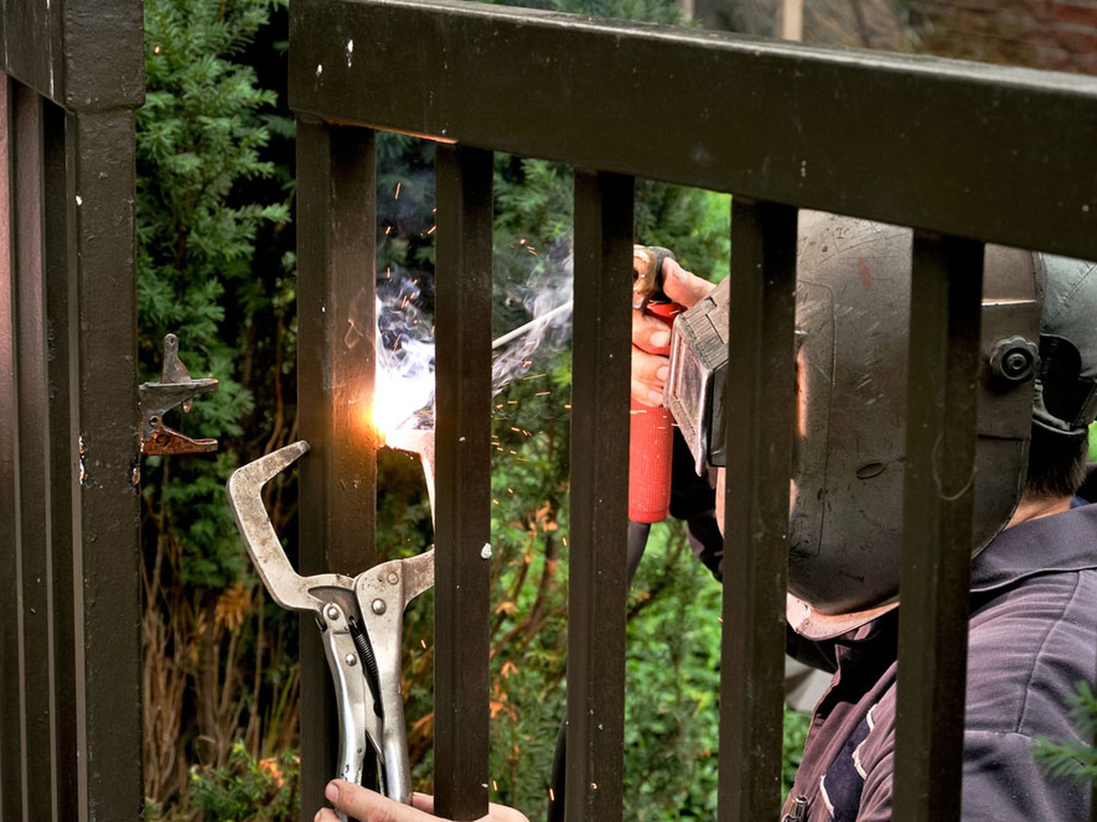 Welder repairing a cracked joint on a metal gate frame, clamped with locking pliers