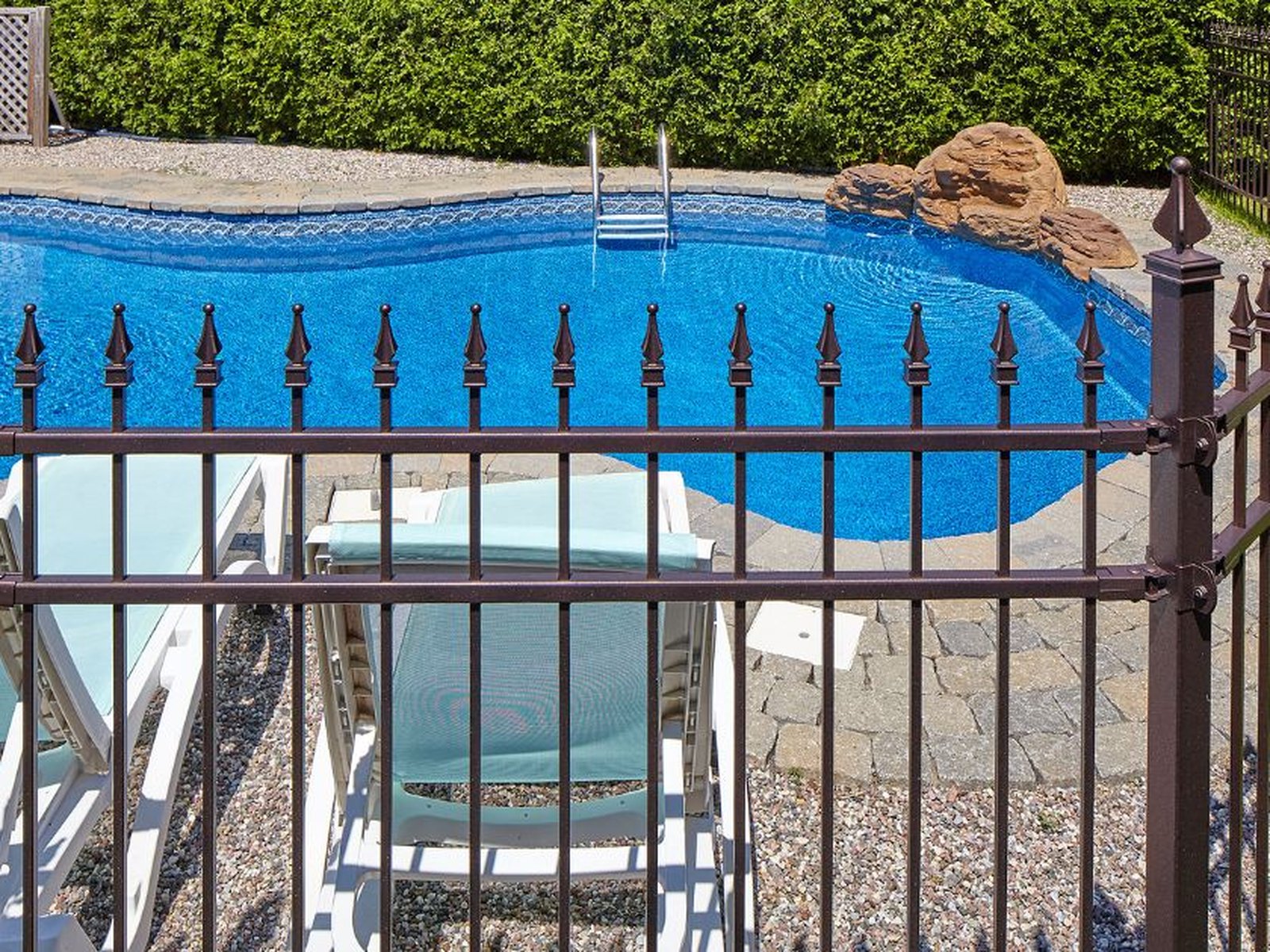 Bronze aluminum pool fence with spear-top pickets enclosing an in-ground pool