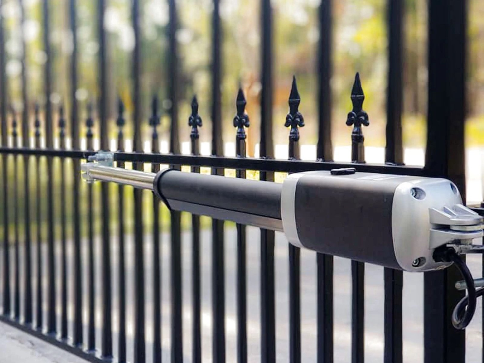 Linear swing arm gate operator mounted to the frame of a black ornamental iron gate