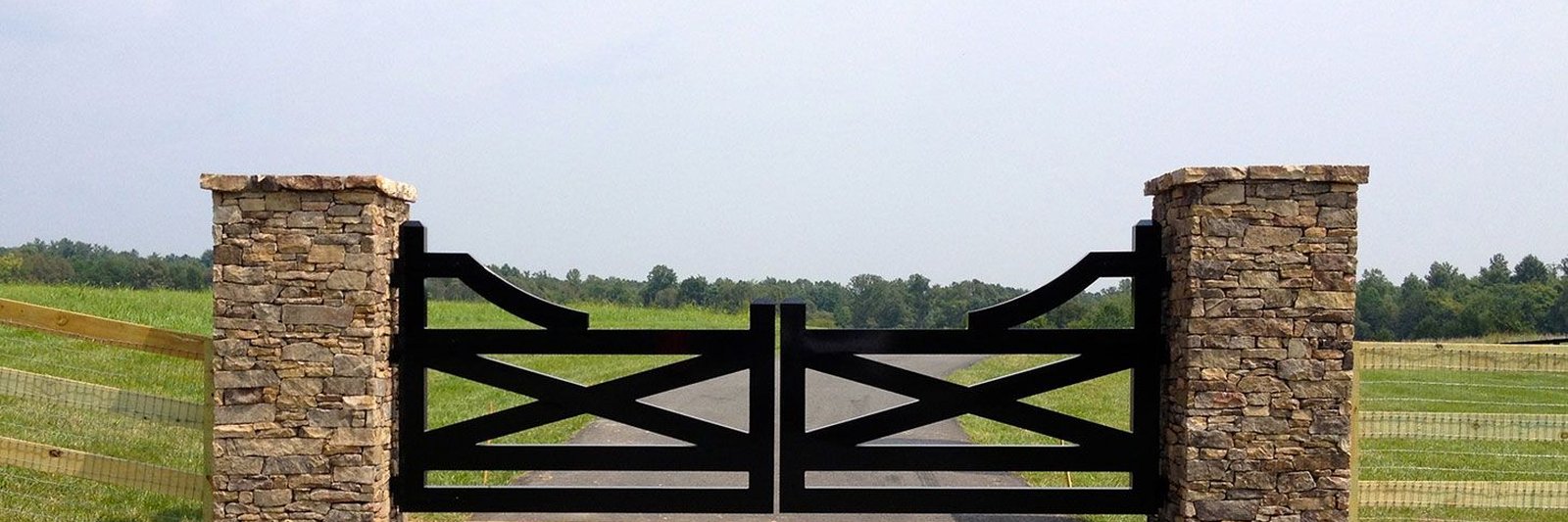 Iron entry gate between dry-stacked stone columns at a ranch driveway