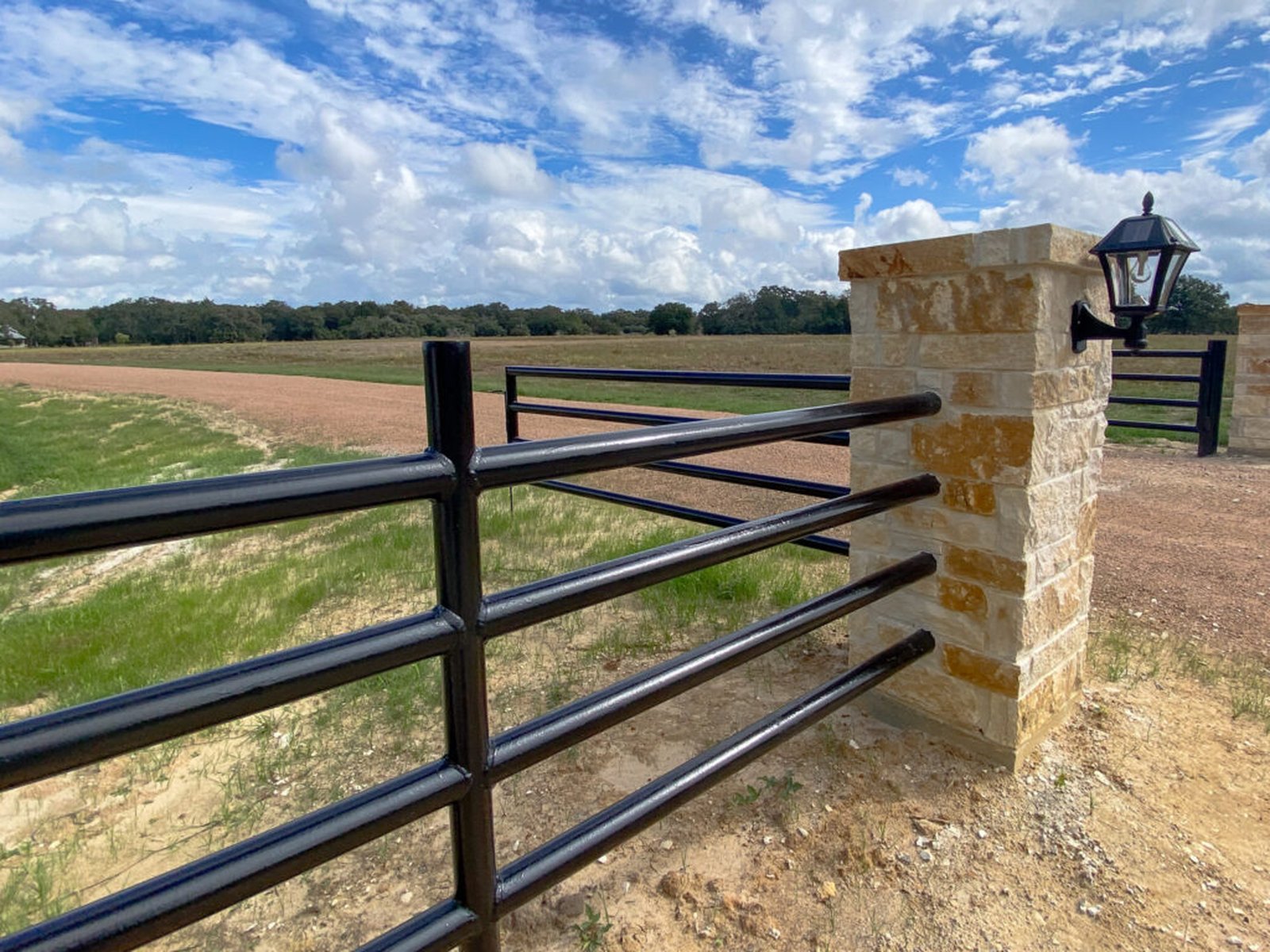 Four-rail black pipe fence running to a limestone entrance column