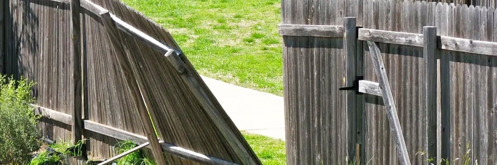 Weathered wood fence with one section collapsed outward and another leaning, both propped with scrap lumber