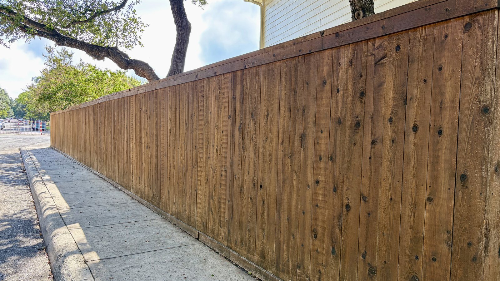 Stained wood privacy fence along a sidewalk with the smooth side facing the street and a cap rail on top