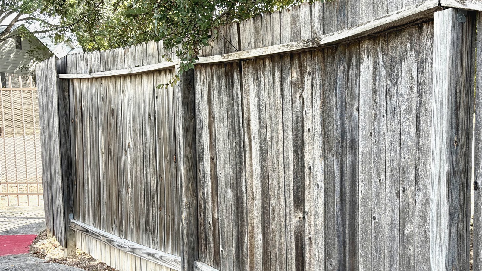 Weathered wood fence installed with the horizontal rails and posts facing the street rather than the yard