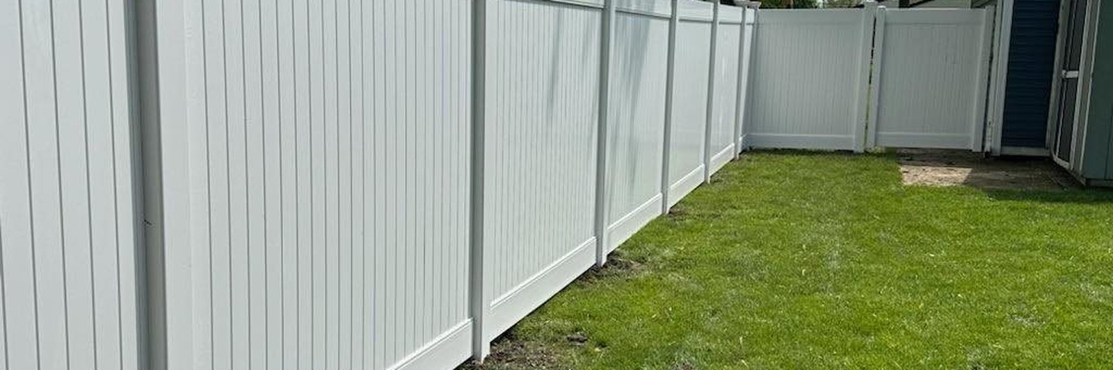 White vinyl privacy fence panels installed along a residential property line