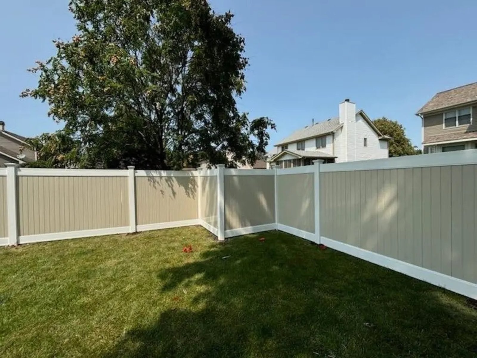 Tan vinyl privacy fence with white posts turning a corner in a back yard